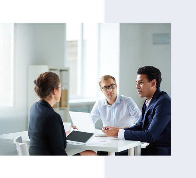Three business professionals having a meeting around a table in a bright office, with laptops open in front of them.