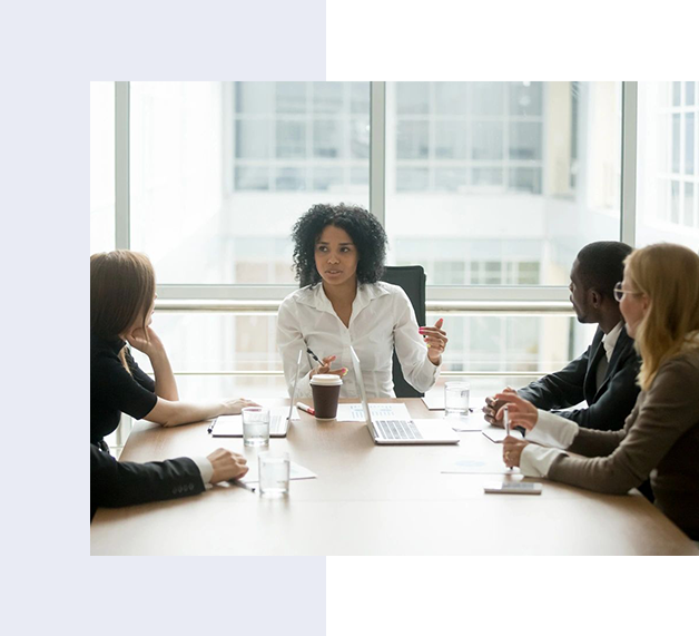 A woman in a white shirt leads a meeting with three colleagues seated around a conference table in a modern office setting.